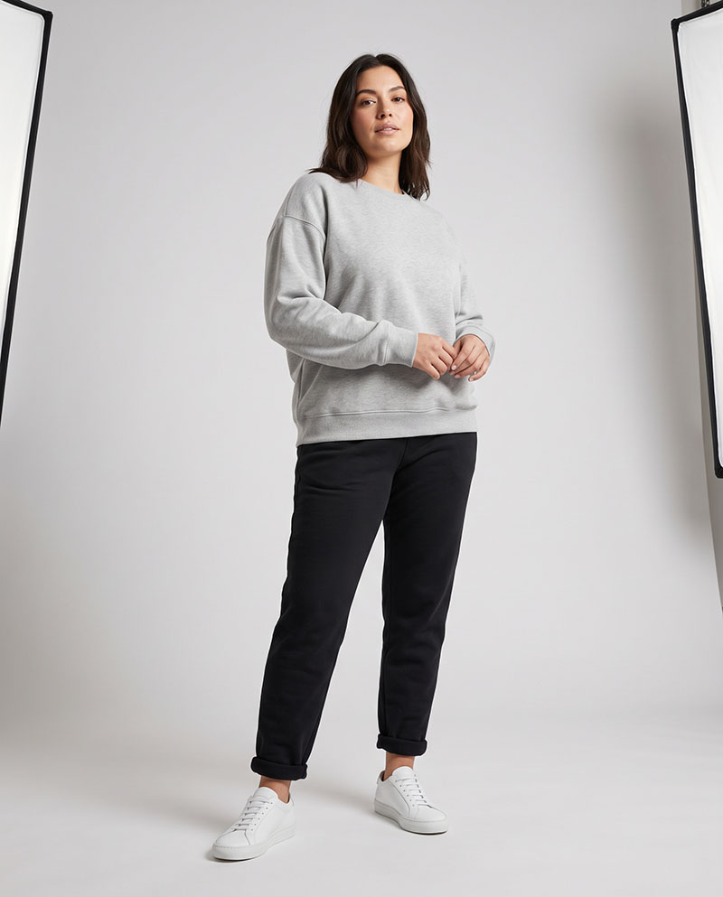 Female model wearing a gray relaxed crewneck sweatshirt in a full-body studio shot, showing brushed fleece comfort and dropped-shoulder fit