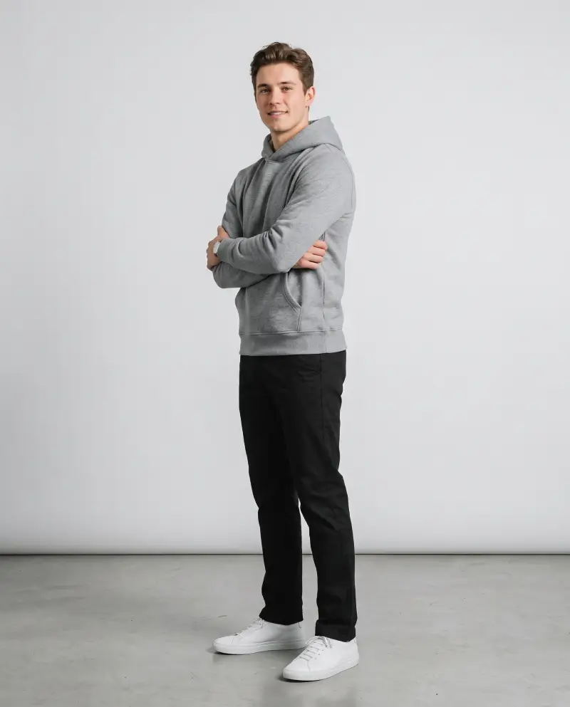 Full-body shot of a male model wearing a gray hoodie solo with black straight-leg pants and white sneakers, street style look