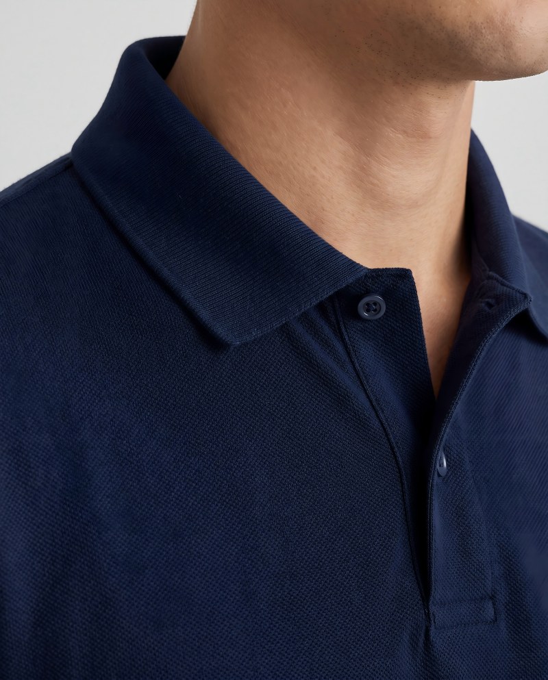 Close-up of a man wearing a navy pique polo shirt, crisp ribbed collar and visible textured cotton weave.