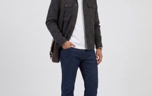 Full-body shot of a male model wearing a work jacket with a tee and jeans, commuter look